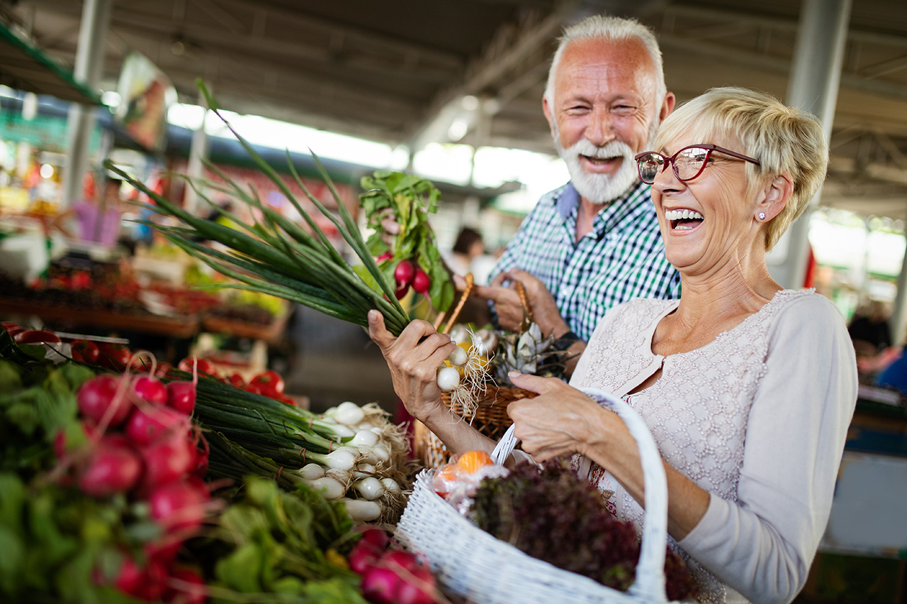 Smiling senior couple holding a basket with vegetables at the market